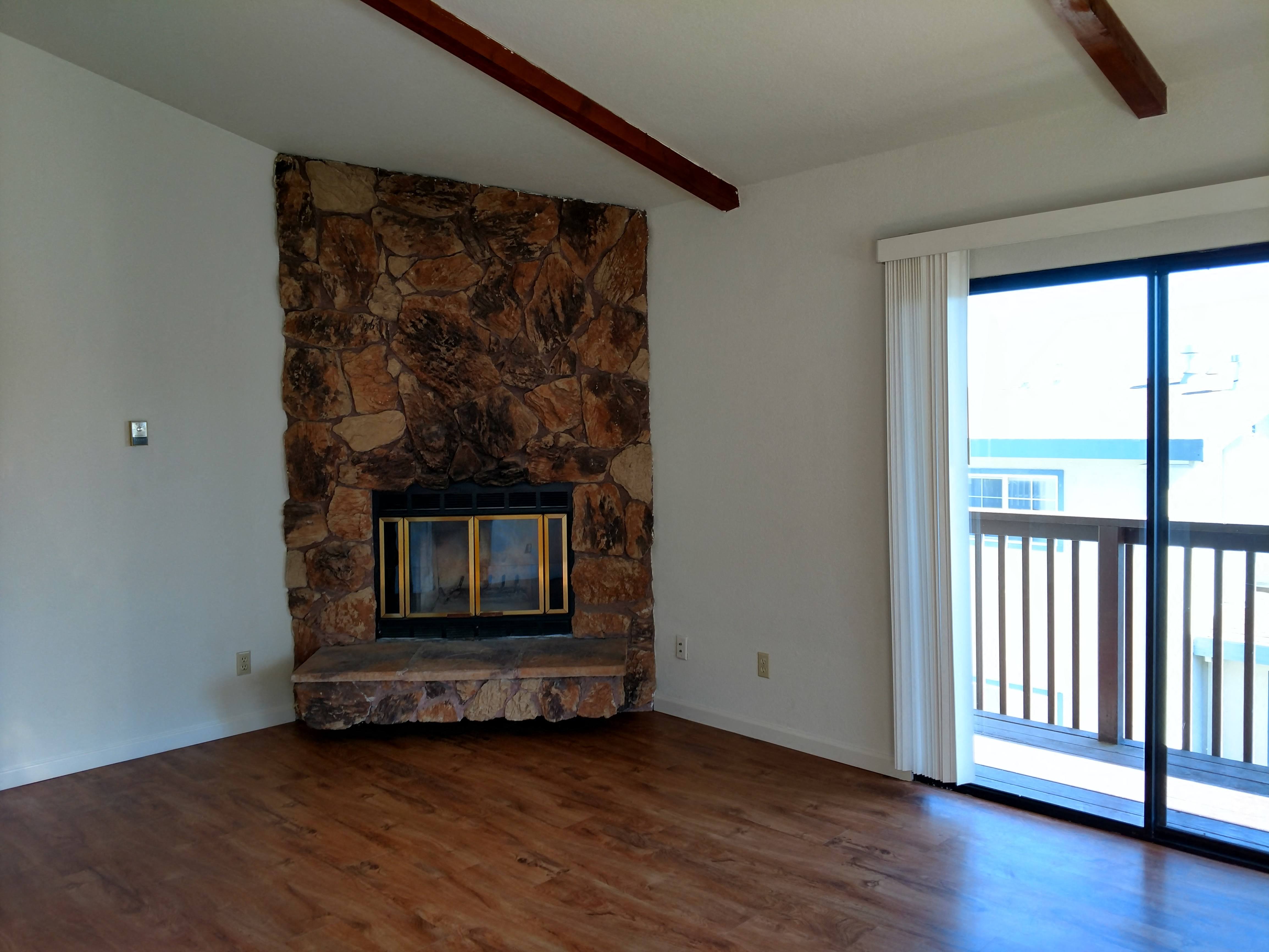 an empty living room with a stone fireplace and wood floors